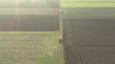 Yörüngenin üstünde, doli hareketli, traktör manzaralı, içi kimyasal içerikli içi doldurulmuş çuvallarla dolu bir römorku sürüklüyor, kırsal yolda giderken, yapay gübre yaymak için monte edilmiş bir makineyi takip ediyor..