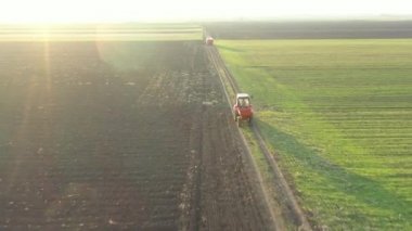 Yörüngenin üstünde, doli hareketli, traktör manzaralı, içi kimyasal içerikli içi doldurulmuş çuvallarla dolu bir römorku sürüklüyor, kırsal yolda giderken, yapay gübre yaymak için monte edilmiş bir makineyi takip ediyor..
