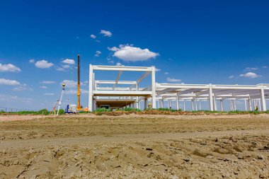 Mobil vinç endüstriyel binanın beton iskeletini monte ediyor, makinelerle, insanlar çalışıyor. İnşaat alanında lazer seviyelendirme diğer cihazlara sahip toplam merkez aygıt.