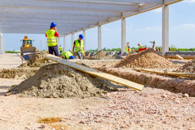 Ahşap kalas inşaat alanındaki kum yığınına konur. Riggers, işçiler siper hazırlıyor, çakıl seviyesini yeniden hizalamak için kürek kullanıyorlar, temel somut kalıplar olarak..