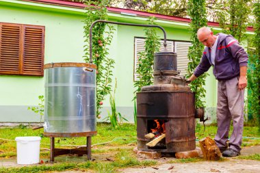 Adam manuel olarak el ile bakırdan yapılmış el yapımı içki imalathanesinde meyve markı karıştırmak, kaçak içki, brendi, konyak, viski, viski, viski, viski, cin, viski gibi alkollü içecekler yapmak için kolu çeviriyor..