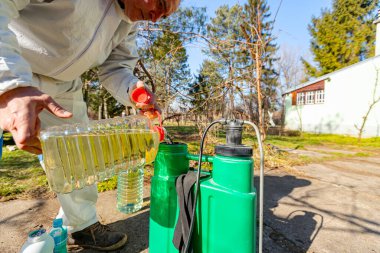 Çiftçi, meyve ağaçlarını mantar veya haşarat hastalıklarından korumak için meyve suyu püskürtmek için plastik sırt çantasındaki böcek ilacının su ve botanik çözeltilerini hazırlıyor..