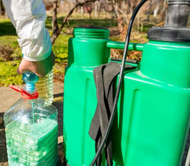 Çiftçi, meyve ağaçlarını mantar veya haşarat hastalıklarından korumak için meyve suyu püskürtmek için plastik sırt çantasındaki böcek ilacının su ve botanik çözeltilerini hazırlıyor..