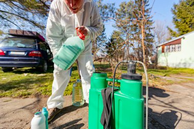 Çiftçi, meyve ağaçlarını mantar veya haşarat hastalıklarından korumak için meyve suyu püskürtmek için plastik sırt çantasındaki böcek ilacının su ve botanik çözeltilerini hazırlıyor..