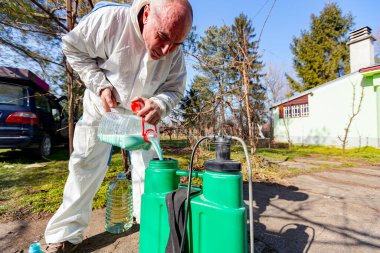 Çiftçi, meyve ağaçlarını mantar veya haşarat hastalıklarından korumak için meyve suyu püskürtmek için plastik sırt çantasındaki böcek ilacının su ve botanik çözeltilerini hazırlıyor..