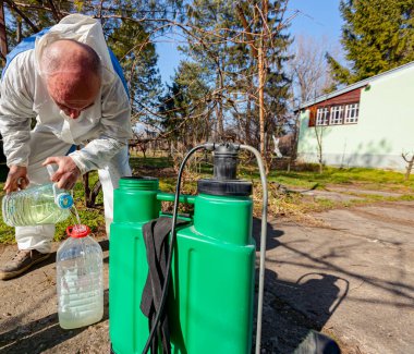 Çiftçi, meyve ağaçlarını mantar veya haşarat hastalıklarından korumak için meyve suyu püskürtmek için plastik sırt çantasındaki böcek ilacının su ve botanik çözeltilerini hazırlıyor..
