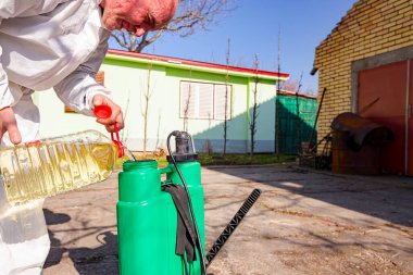 Çiftçi, meyve ağaçlarını mantar veya haşarat hastalıklarından korumak için meyve suyu püskürtmek için plastik sırt çantasındaki böcek ilacının su ve botanik çözeltilerini hazırlıyor..