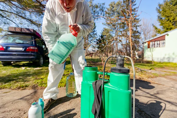 Çiftçi, meyve ağaçlarını mantar veya haşarat hastalıklarından korumak için meyve suyu püskürtmek için plastik sırt çantasındaki böcek ilacının su ve botanik çözeltilerini hazırlıyor..