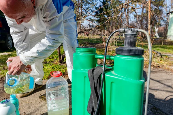 Çiftçi, meyve ağaçlarını mantar veya haşarat hastalıklarından korumak için meyve suyu püskürtmek için plastik sırt çantasındaki böcek ilacının su ve botanik çözeltilerini hazırlıyor..