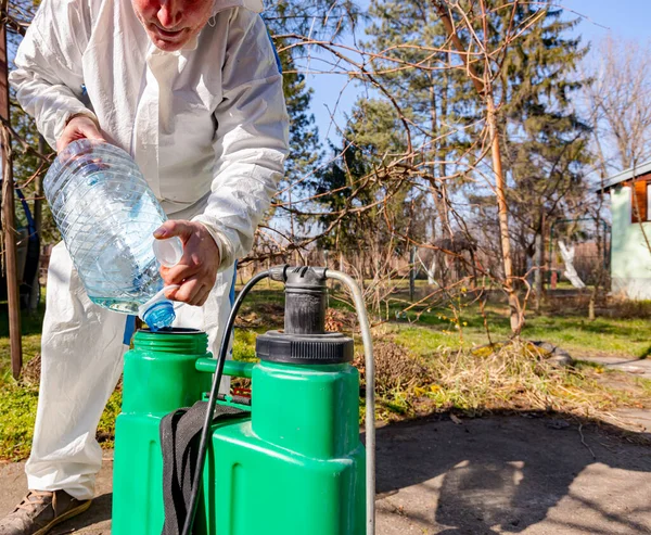 Çiftçi, meyve ağaçlarını mantar veya haşarat hastalıklarından korumak için meyve suyu püskürtmek için plastik sırt çantasındaki böcek ilacının su ve botanik çözeltilerini hazırlıyor..