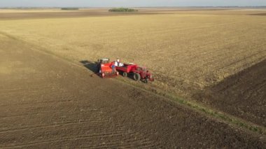 İki çiftçi, yeni buğday ekmeleri için içi doldurulmuş tahıl tohumlarıyla elle ekme makinesini doldururken, yukarıda yörüngede dolanıyorlar..