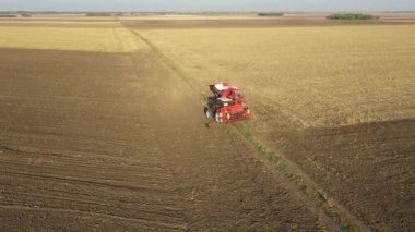 İki çiftçi, yeni buğday ekmeleri için içi doldurulmuş tahıl tohumlarıyla elle ekme makinesini doldururken, yukarıda yörüngede dolanıyorlar..