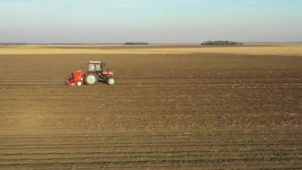 横ビューの上に 可鍛性フィールド 新しい小麦の作物を植える上に種子ドリルマシンを引っ張るトラクターのドリー移動 — ストック動画