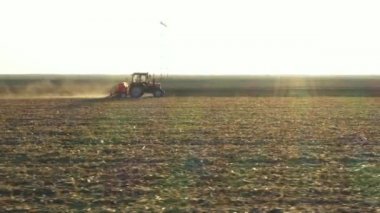 Yan görünümün üstünde, çekici, tohum makinesini tarla, toprak ve yeni buğday ekimi üzerine çeker gibi hareket ettirir..