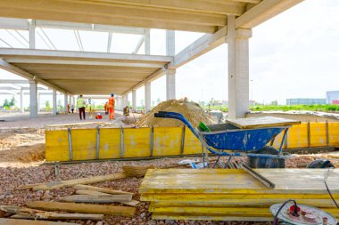 İnşaat alanında istiflenmiş, boyanmış, ahşap tahtalarla kullanılmış el arabasının görüntüsü. Riggers ve işçiler somutlaştırma için uzun kalıplar oluşturuyorlar.