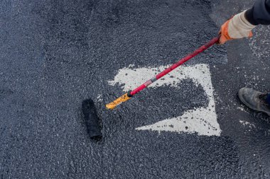 Worker is coating tarmac using a brush roller, apply the first basic protective layer of waterproofing.