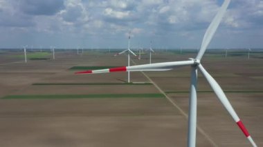 Above view, dolly move, over farm of large wind power turbines are standing among agricultural fields, generating clean renewable electrical energy for sustainable development.