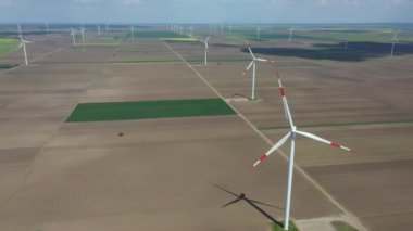 Above view, dolly move, over farm of large wind power turbines are standing among agricultural fields, generating clean renewable electrical energy for sustainable development.