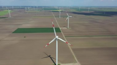 Above view on farm of large wind power turbines are standing among agricultural fields, generating clean renewable electrical energy for sustainable development.