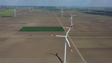 Above view, dolly move, over farm of large wind power turbines are standing among agricultural fields, generating clean renewable electrical energy for sustainable development.
