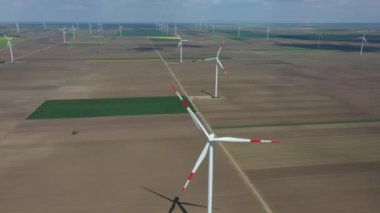 Above view, dolly move, over farm of large wind power turbines are standing among agricultural fields, generating clean renewable electrical energy for sustainable development.