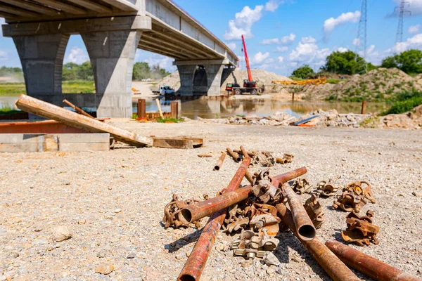 View on a heap of corrosion pipes disassembled steel scaffold joints placed on the ground at the construction site, bridge is in the background.