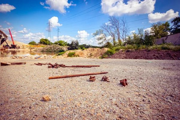 View on a heap of corrosion pipes disassembled steel scaffold joints placed on the ground at the construction site, bridge is in the background.