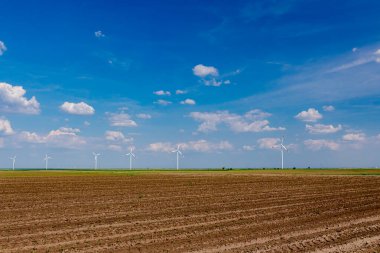 Birkaç büyük rüzgar enerjisi türbininin çiftliği tarım alanlarının arasında duruyor ve temiz yenilenebilir elektrik enerjisi üretiyorlar.