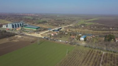 Manzaranın üstünde, doli hareket, inşaat alanının üstünde, döner kavşak ve yol tamamlanmamış köprünün üzerinden geçiyor, makineleşme, inşaat halindeki nehrin üzerinden. Birkaç metal silosu olan tarım sanayi bölgesi.