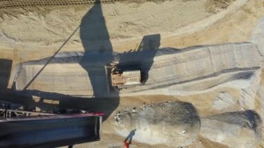 Üst tarafta, kargoyu boşaltmak için karavanını kaldırırken, üst tarafta, buldozer sürüngeninin ittiği, inşaat sahasında düzleştirdiği küçük, ezilmiş taş var..