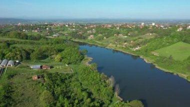 Manzaranın üstünde, göl, orman, dağ manzarası kır evi yerleşimi, ekili, ekilebilir araziler üzerinde çeşitli seralar, kirli yollar göl kenarındaki orman ağaçlarının arasına uzanıyor..