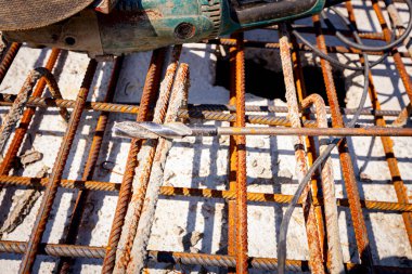 İnşaat alanındaki köprünün dayanıklılığı için döşenmiş paslı kare takviye ağlarına beton döşemek için elle öğütücü ve matkap..