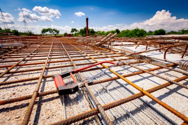 İnşaat alanındaki köprünün dayanıklılığı için döşenmiş paslı kare güçlendirme ağlarına yerleştirilmiş bir demir testeresi..