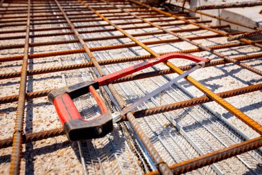 İnşaat alanındaki köprünün dayanıklılığı için döşenmiş paslı kare güçlendirme ağlarına yerleştirilmiş bir demir testeresi..