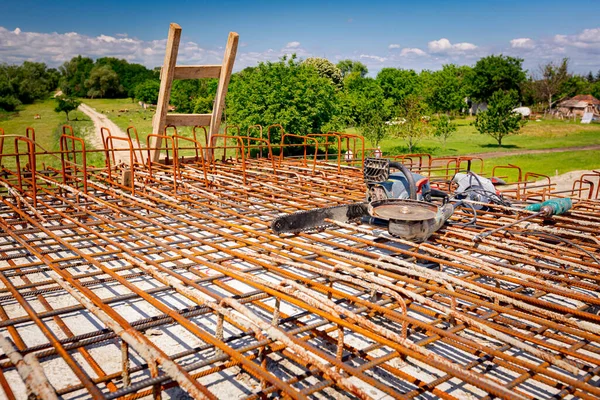 Ladder, chainsaw, manually electrical grinder and drill for concrete are set on rusty square reinforcing mesh that was placed for the strength of the bridge on the construction site.