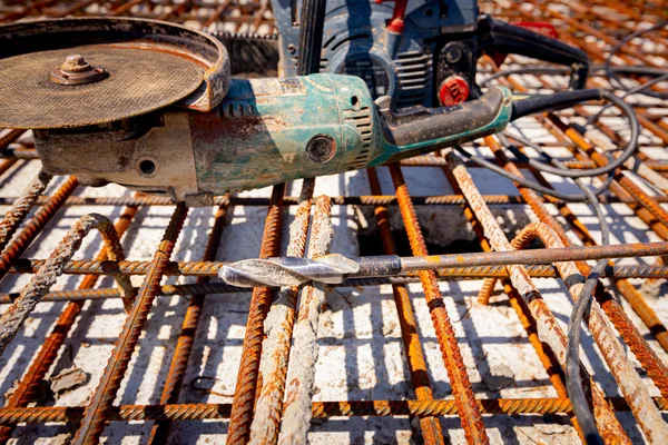 A manually electrical grinder and  drill for concrete set on rusty square reinforcing mesh that was placed for the strength of the bridge on the construction site.