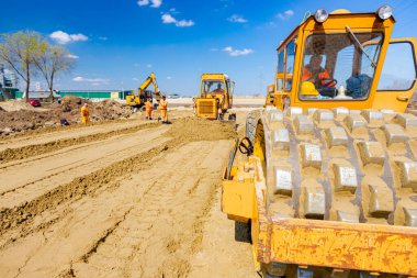 Dikenli ve buldozerli yol silindiri, inşaat alanındaki yol temeli için kum seviyesini düşürüyor..