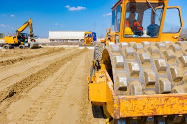 Dikenli ve buldozerli yol silindiri, inşaat alanındaki yol temeli için kum seviyesini düşürüyor..