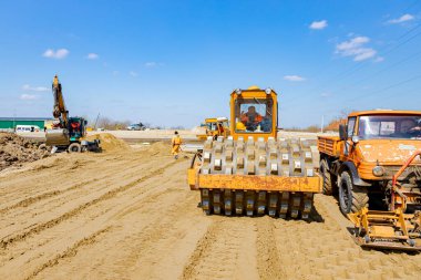 Çivili yol silindiri ve plaka titreşim sıkıştırıcılı kamyon inşaat alanındaki yol temeli için kumu düzleştiriyor..