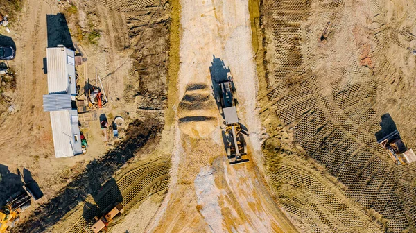 Above top view on the building site with mechanization, roundabout under construction with road that goes over unfinished bridge.