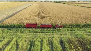 Above view, dolly move backward, tractor with two trailers is waiting as agricultural harvester is cutting and harvesting mature sunflower on farm fields.