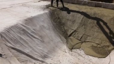 Construction worker is directing the pump tube on right direction, pouring first layer of concrete in building foundation.