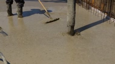 Riggers, workers are using rake to leveling concrete after pump tube is pouring in building foundation over reinforcing steel bars.