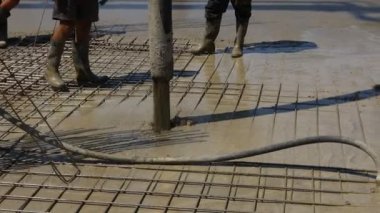 Pump hose is pouring fresh concrete in the base of new building covering square reinforcement.