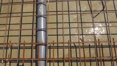 Fresh liquid concrete is flowing slowly under square reinforcement in the base of new building covering sanitary pipeline, set of embed plastic pipes for sewer.