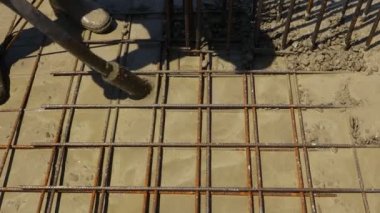 Worker is using power tool, compactor, for compacting fresh liquid concrete, flowing slowly among square reinforcement in the base of new building.