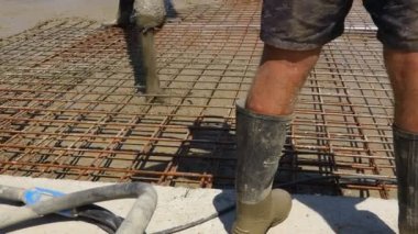 Pump hose is pouring fresh concrete in the base of new building covering square reinforcement.