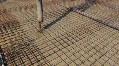 Pump hose is pouring fresh concrete over square reinforcement in the base of new building covering sanitary pipeline, set of embed plastic pipes for sewer.