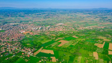 Yeşil tepe manzarasının üzerinde çekilmiş, uzaktaki orman ağaçları ve şehirler arasında ekilmiş araziler..