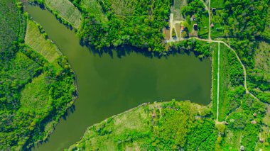 Above top view, overhead, on the end of the lake surrounded by green forest and several cultivated plots with cottages.
